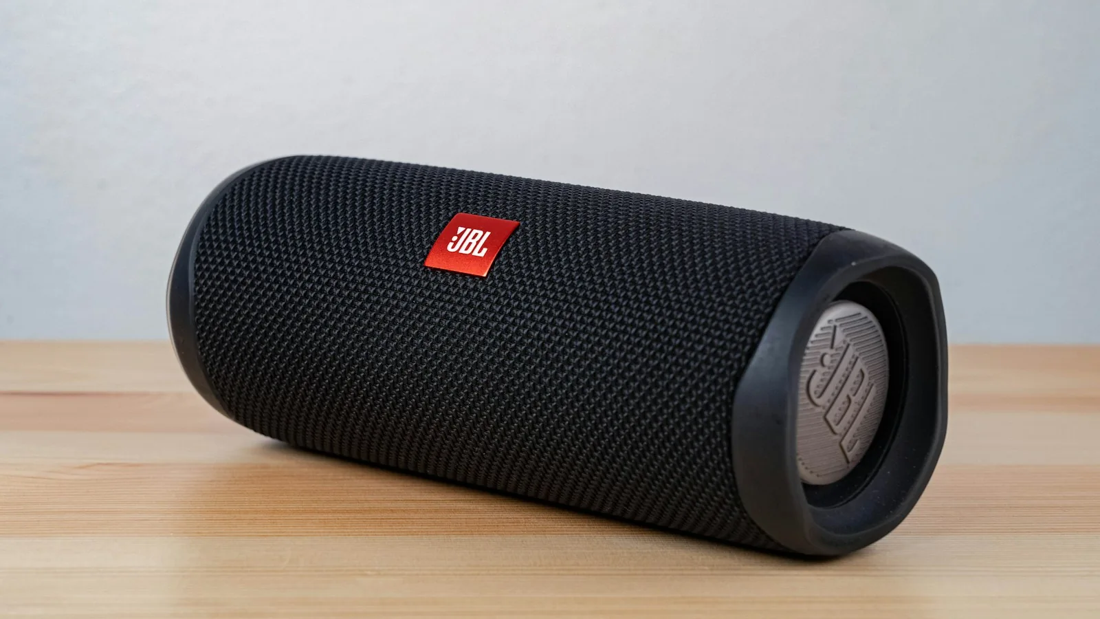 Black cylindrical JBL portable speaker on a timber surface