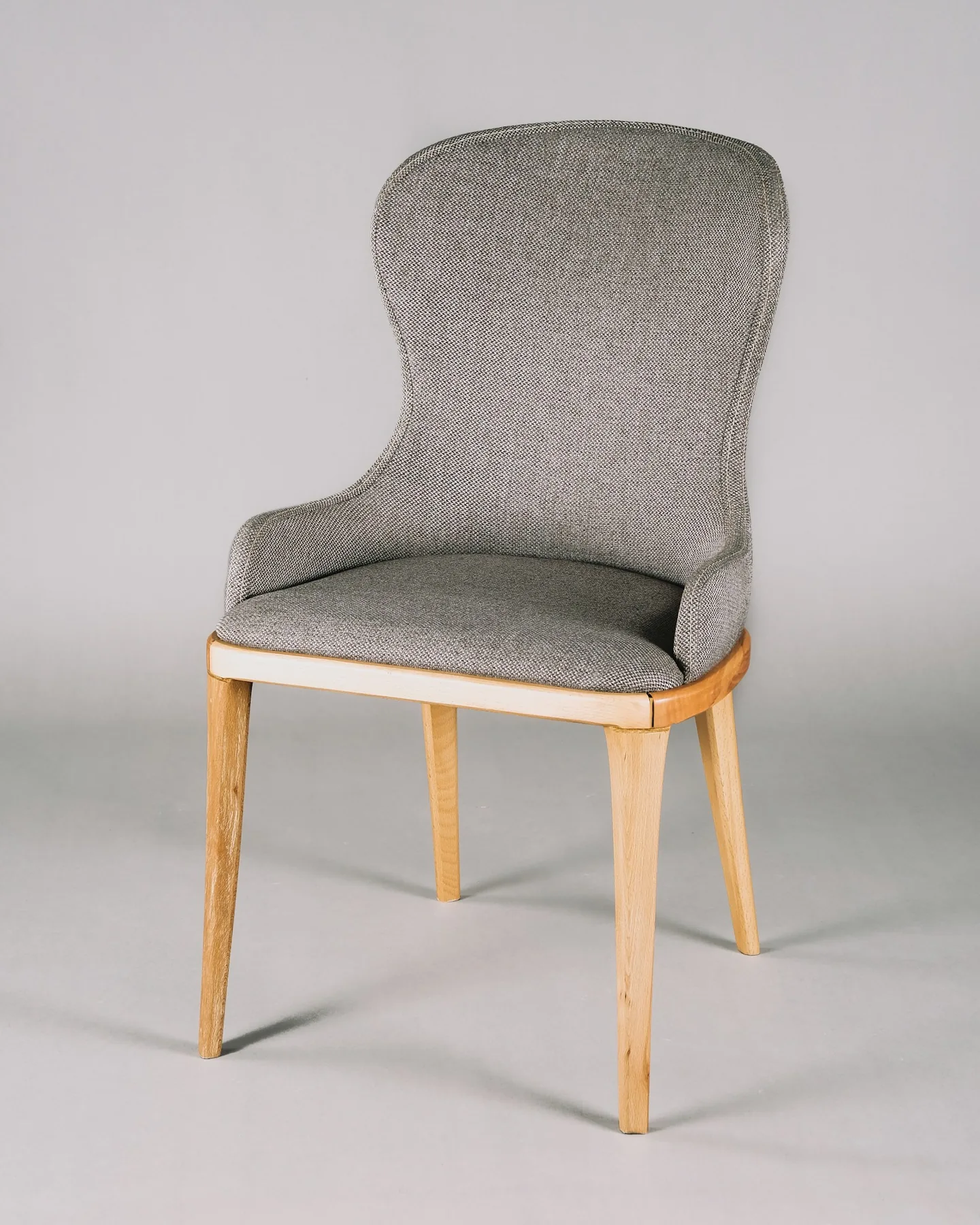 Upholstered Scandinavian chair with a pale oak frame against a warm grey wall